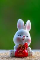 três fofa chinês coelhos boneca segurando uma vermelho dinheiro saco e sorrir com verde natureza borrado fundo. adorável Coelho personagem desenhos para meio outono festival, ano do a Coelho 2023, e Páscoa foto