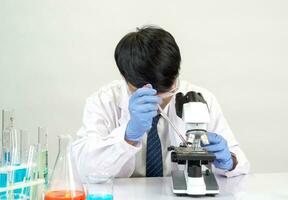 retrato ásia homem aluna cientista vestindo uma médico vestido dentro a laboratório olhando mão às químico. causou de mistura reagentes dentro científico pesquisa laboratórios com teste tubos e microscópio em a mesa foto