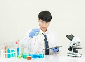 retrato ásia homem aluna cientista vestindo uma médico vestido dentro a laboratório olhando mão às químico. causou de mistura reagentes dentro científico pesquisa laboratórios com teste tubos e microscópio em a mesa foto