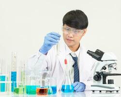 retrato ásia homem aluna cientista vestindo uma médico vestido dentro a laboratório olhando mão às químico. causou de mistura reagentes dentro científico pesquisa laboratórios com teste tubos e microscópio em a mesa foto