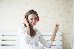 linda mulher ouvindo música de manhã sentada na cama em casa foto