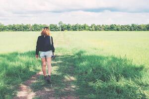 costas de mulher jovem carregando câmera retro no campo de grama divirta-se foto