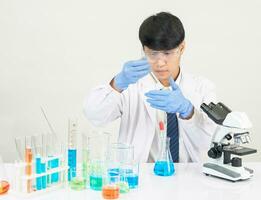 retrato ásia homem aluna cientista vestindo uma médico vestido dentro a laboratório olhando mão às químico. causou de mistura reagentes dentro científico pesquisa laboratórios com teste tubos e microscópio em a mesa foto