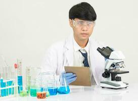 retrato ásia homem aluna cientista vestindo uma médico vestido dentro a laboratório olhando mão às químico. causou de mistura reagentes dentro científico pesquisa laboratórios com teste tubos e microscópio em a mesa foto