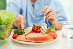 ásia idosos mulher paciente comendo salmão estaca e vegetal salada para saudável Comida dentro hospital. foto