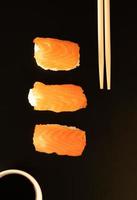 sushi com salmão e pauzinhos isolados no fundo preto foto