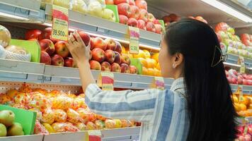 retrato do uma lindo ásia ou indonésio mulher comprando fruta arranjado em fruta prateleira dentro uma supermercado foto