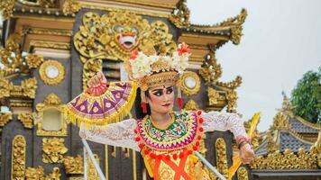 menina vestindo balinesa tradicional vestir com uma dançando gesto em balinesa têmpora fundo com portátil fã, coroa, joia, e ouro enfeite acessórios. balinesa dançarino mulher retrato foto