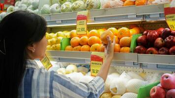 retrato do uma lindo ásia ou indonésio mulher comprando fruta arranjado em fruta prateleira dentro uma supermercado foto