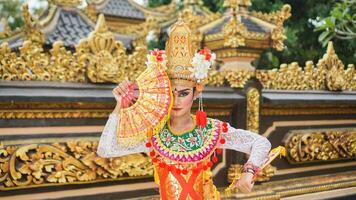 menina vestindo balinesa tradicional vestir com uma dançando gesto em balinesa têmpora fundo com portátil fã, coroa, joia, e ouro enfeite acessórios. balinesa dançarino mulher retrato foto