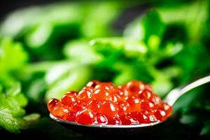 uma cheio colherada do vermelho caviar em a mesa com salsinha. foto