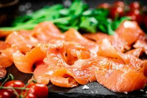 salgado salmão em uma pedra borda com tomates e verdes. foto