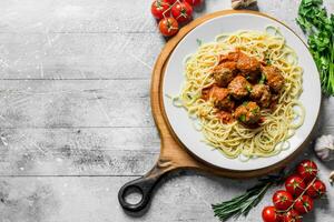 espaguete e carne bolas em uma prato com tomates, ervas e alho. foto