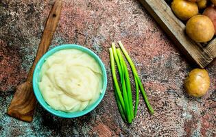 amassado batatas dentro uma tigela com verde cebolas . foto