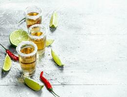 tequila dentro uma tiro vidro com fatias do Lima e vermelho quente Pimenta. foto