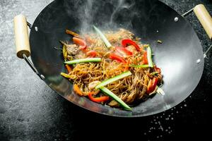 quente celofane Macarrão dentro uma fritar panela wok com Sino pimentas, pepino e cenouras. foto