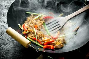 quente wok chinês celofane Macarrão dentro uma panela com uma espátula. foto