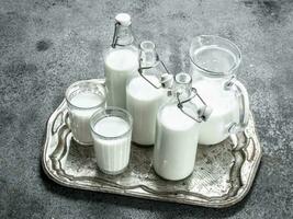 fresco leite dentro garrafas, jarros e óculos em uma aço bandeja. foto
