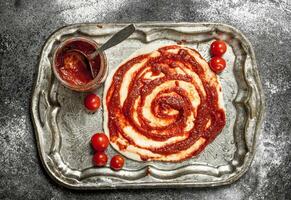 preparação do pizza. inscrição do tomate molho em a enrolado massa. foto