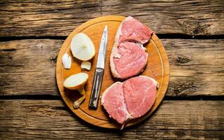 peças do cru carne com cebolas em uma cortar borda. foto