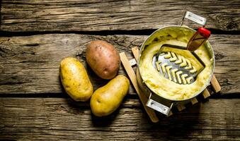 cozinhando amassado batatas com pilão em de madeira fundo. foto