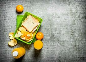 sanduíches, laranja suco e fruta. em a pedra mesa foto