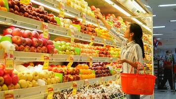 retrato do uma lindo ásia ou indonésio mulher comprando fruta arranjado em fruta prateleira dentro uma supermercado foto