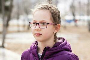 jovem atraente sério menina dentro óculos dentro uma cidade parque dentro cedo Primavera parece para dentro a distância foto