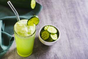 desintoxicação pepino limonada dentro uma vidro com uma Palha e uma pepino em a mesa foto