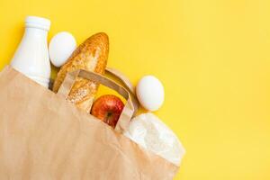 Comida Entrega conceito. pão, leite, ovos, cereais e frutas dentro uma papel saco em uma amarelo fundo foto