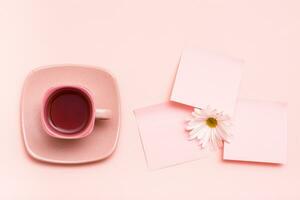 a conceito é Rosa. Rosa beber dentro uma café xícara, folha para escrevendo e crisântemo em uma Rosa fundo. topo Visão foto