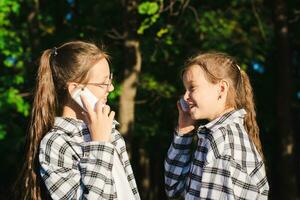 dois alegre meninas falando em despejo telefones dentro uma ensolarado verão parque foto