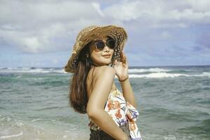 uma feliz jovem ásia mulher vestindo de praia chapéu é posando para a Câmera às a de praia dentro gunungkidul, Indonésia foto