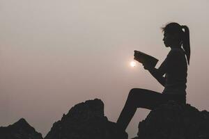 mulheres em pé segurando a bíblia sagrada para adorar a deus no fundo do pôr do sol, rezar para o deus, conceito de silhueta cristã. foto