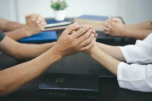 grupo do pessoas segurando mãos dentro lembrança do Deus em a mesa lá é uma Bíblia, respeito, espiritualidade e religião. cristão fundo Educação procurando ou estudando a Bíblia. foto