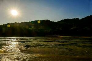 Sol brilhando sobre a rio dentro frente do uma floresta foto