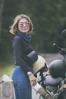 bonita mulher segurando segurança capacete em pé ao lado pequeno enduro motocicleta foto