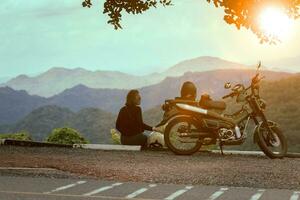 mulher sentado ao lado motocicleta às lindo ponto de vista e olhando para pôr do sol cena foto