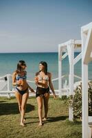 sorridente jovem mulheres dentro bikini desfrutando período de férias em a de praia foto