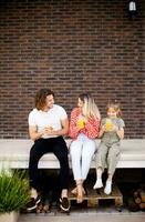 família com uma mãe, pai e filha sentado lado de fora em a passos do uma frente varanda do uma tijolo casa foto