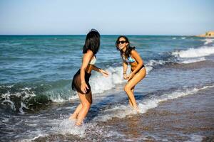 dois bonita jovem mulher tendo Diversão em a beira-mar foto