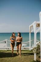 sorridente jovem mulheres dentro bikini desfrutando período de férias em a de praia foto