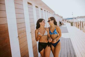 sorridente jovem mulheres dentro bikini desfrutando período de férias em a de praia foto