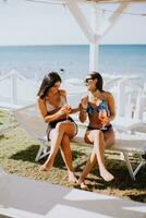 sorridente jovem mulheres dentro bikini desfrutando período de férias em a de praia foto