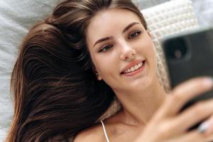 mulher encantada usando smartphone na cama foto