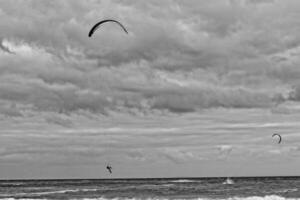 verão panorama com a oceano com Sombrio nublado ondas e surfista kit com pára-quedas flutuando em a costa foto
