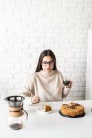 mulher sentada à mesa branca, comendo bolo e tomando café foto