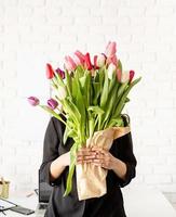 mulher de negócios em pé ao lado da mesa com um buquê de tulipas frescas foto