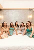 uma grupo do ásia mulheres dentro lindo vestidos sentado juntos em uma branco cama enquanto ficando foto