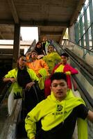 uma grupo do ásia homens dentro limão verde jaquetas estão em pé com seus amigos em a escada rolante foto